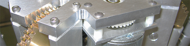 A close up of a piece of aluminum machinery—there are a variety of cogs contained within the thick metal housing.