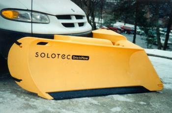 A yellow Solotec snow plow is shown attached to a white truck on a city street.