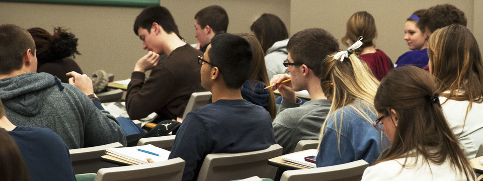 A group of college students in a lecture hall taking notes during a presentation.