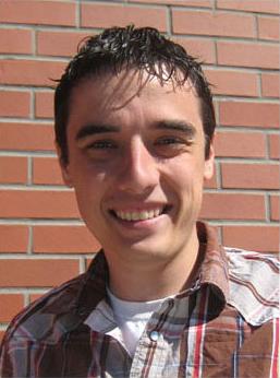 Headshot of Bryan. A brick wall is behind him and he is wearing a brown and white flannel shirt with a white t-shirt.